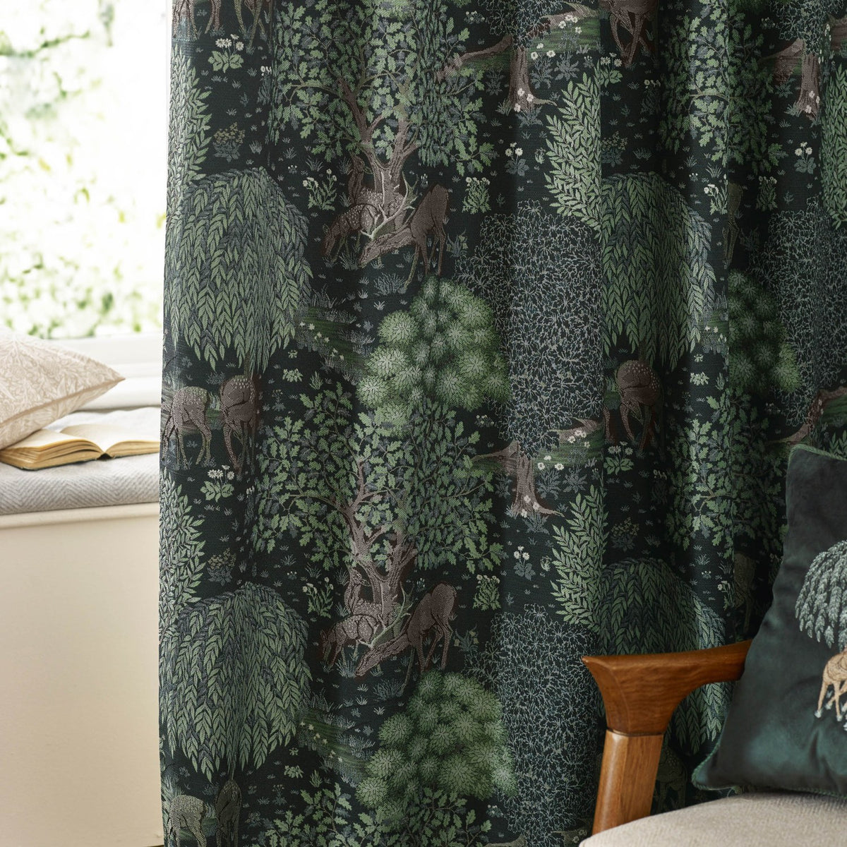 Brook Jacquard pencil pleat curtains in forest green polyester with a woven woodland deer and tree design, shown pleated in a living room setting.