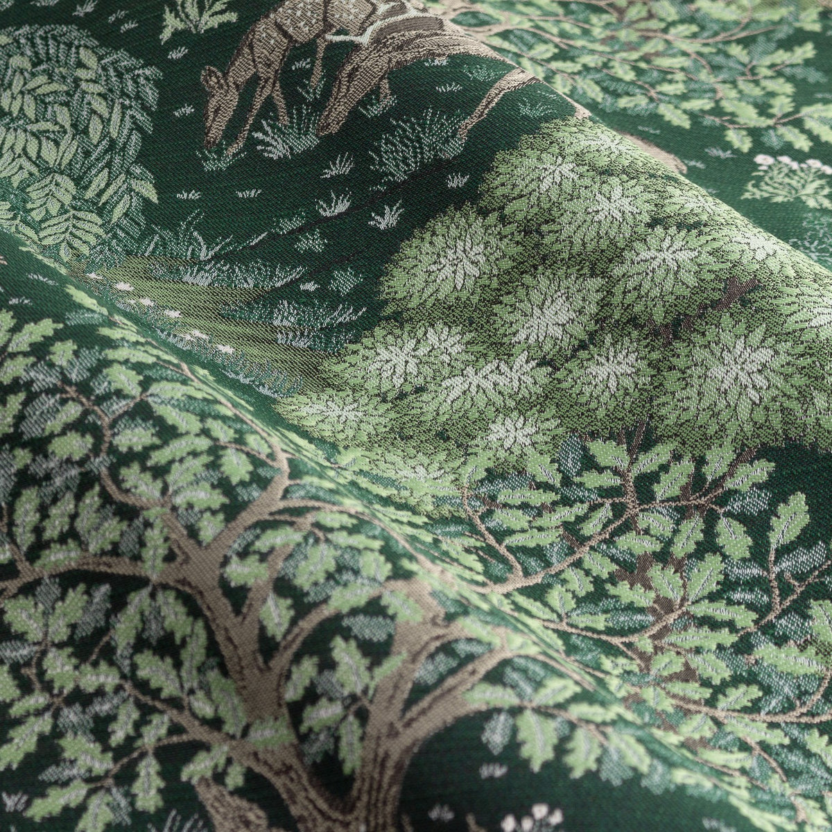 Close-up of Brook Jacquard pencil pleat curtain fabric in forest green, showing a woven woodland scene with deer, trees and foliage in tonal green and beige.
