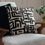 Brooke Abstract Cotton Cushion in Mono, a square cream cotton cushion with black embroidered geometric abstract design, shown on a boucle armchair with wooden arms.