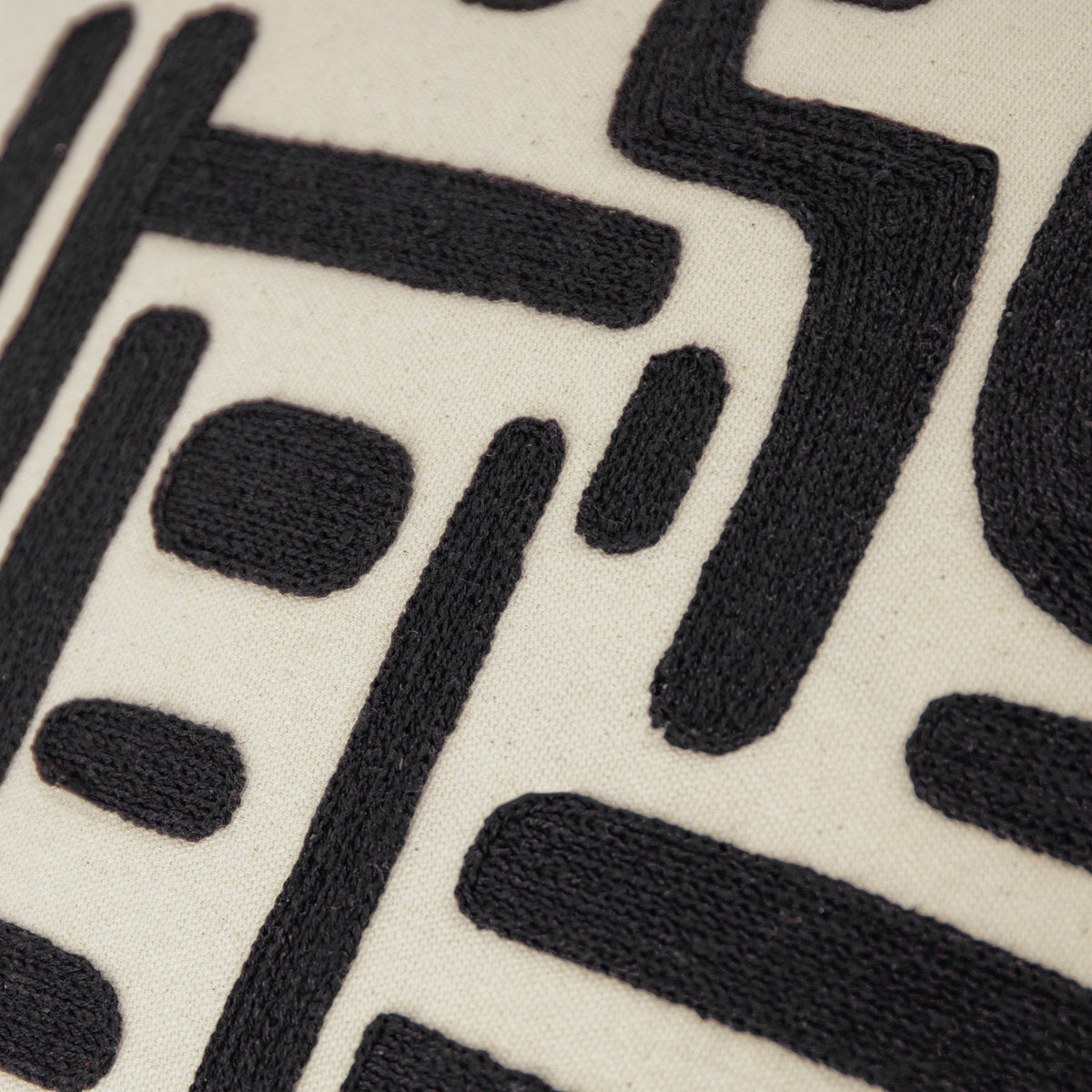 Close-up of the Brooke Abstract Cotton Cushion in Mono, showing black embroidered geometric bars, blocks and curved shapes on natural cream cotton.