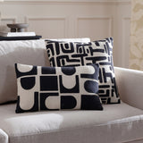 Brooke Abstract Cotton Cushion in Mono, a rectangular cream cotton cushion with black embroidered geometric shapes, shown with a matching square cushion on a light grey sofa.
