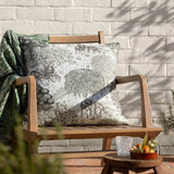The Brook Jacquard Linen Cushion in cream with a green woodland toile of deer and willow trees, styled on a wooden bench beside a folded green throw.