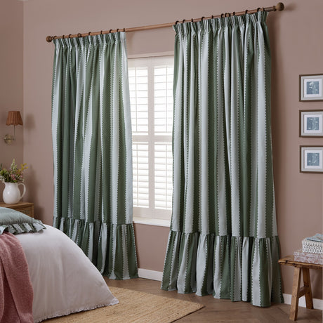 Bay green and mist striped pencil pleat curtains in cotton with scalloped stripe edges and a ruffled hem, shown hung on a wooden pole in a bedroom.