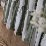 Close-up of Birdie Stripe pencil pleat curtains in bay green and mist, cotton fabric with wavy striped pattern and gathered ruffled hem, pooling on a wooden floor.