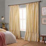 Birdie Stripe Cotton Pencil Pleat Curtains in butter yellow and white stripe with ruffled hem, shown hanging on a wooden pole in a bedroom setting.