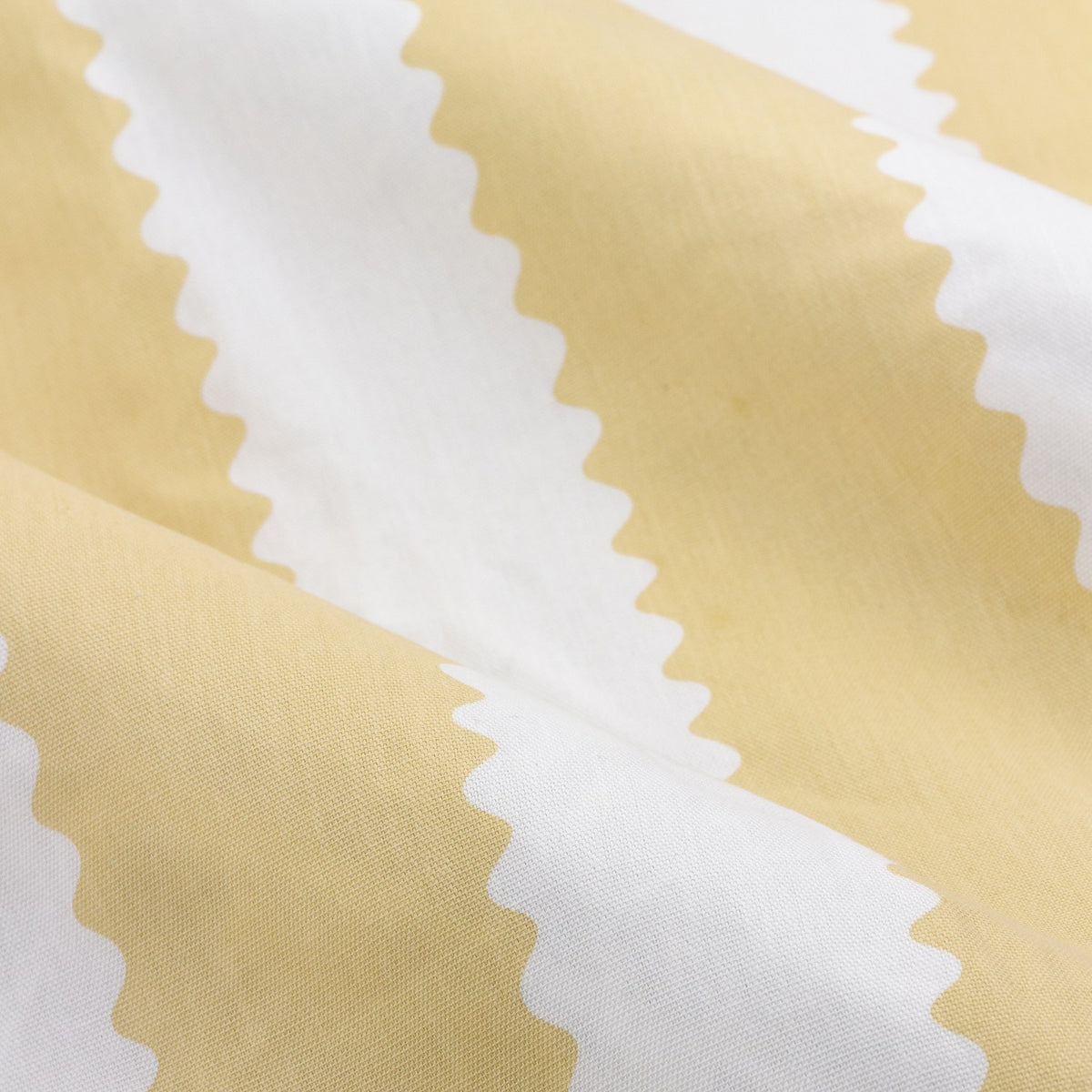 Close-up of Birdie Stripe Cotton Pencil Pleat Curtains showing wavy butter yellow and white stripes on soft, gathered cotton fabric.