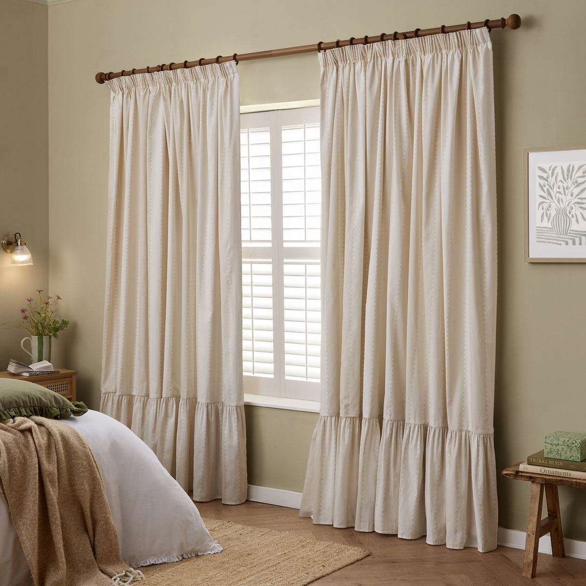 Birdie Stripe pencil pleat curtains in natural cotton with a gathered ruffle hem, shown hung on a wooden pole beside a shuttered window in a bedroom.