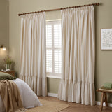 Birdie Stripe pencil pleat curtains in natural cotton with a gathered ruffle hem, shown hung on a wooden pole beside a shuttered window in a bedroom.