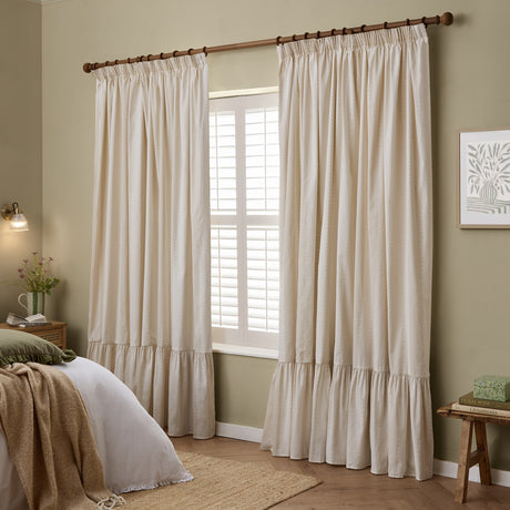 Birdie Stripe pencil pleat curtains in natural cotton with a gathered ruffle hem, shown hung on a wooden pole beside a shuttered window in a bedroom.