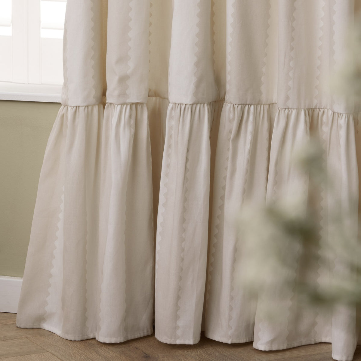 Close-up of Birdie Stripe cotton pencil pleat curtains in natural, showing wavy contrast stripes and a gathered ruffle skirt at the hem, near a window.