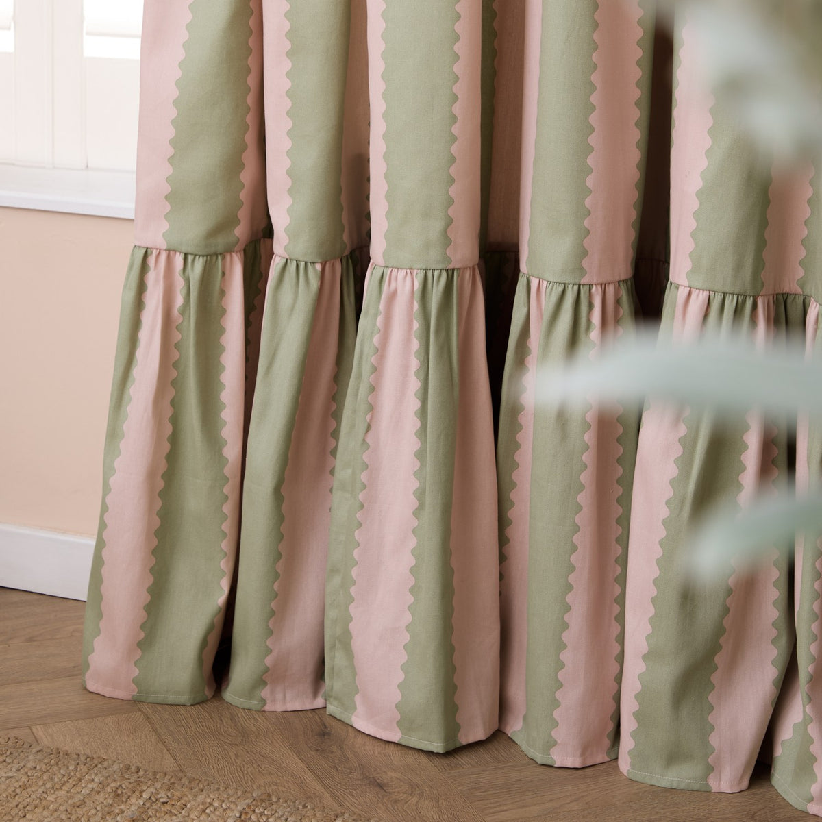 Birdie Stripe Cotton Pencil Pleat Curtains in pink and sage green, showing scalloped-edge vertical stripes and gathered pleat headings against a bedroom window.
