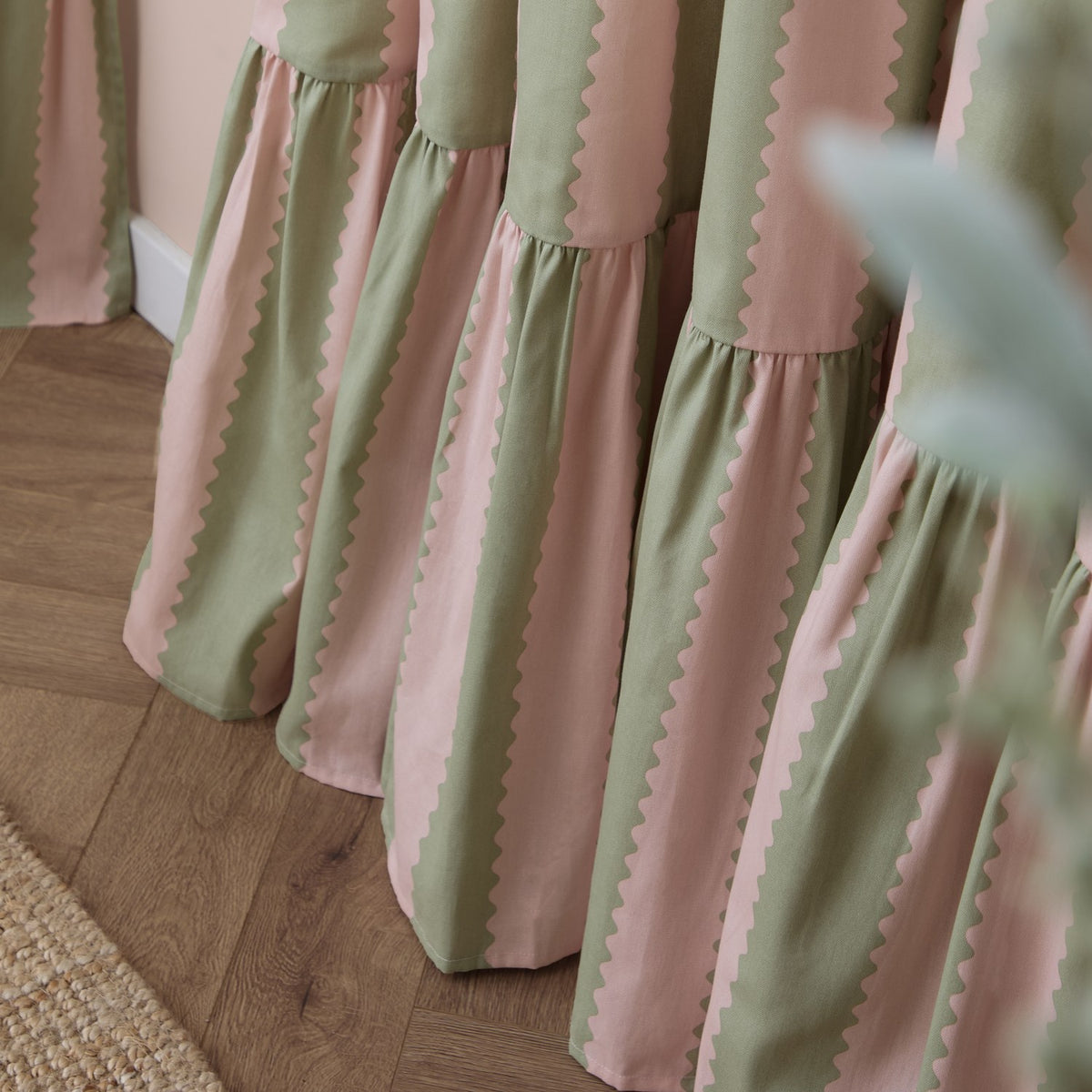 Close-up of Birdie Stripe cotton pencil pleat curtains in pink and sage green, showing wavy scalloped stripe edges and gathered fabric folds.