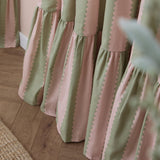 Close-up of Birdie Stripe cotton pencil pleat curtains in pink and sage green, showing wavy scalloped stripe edges and gathered fabric folds.