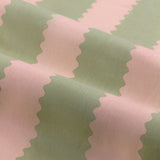 Close-up of Birdie Stripe cotton pencil pleat curtain fabric showing wavy vertical stripes in pink and sage green with a scalloped zig-zag edge.