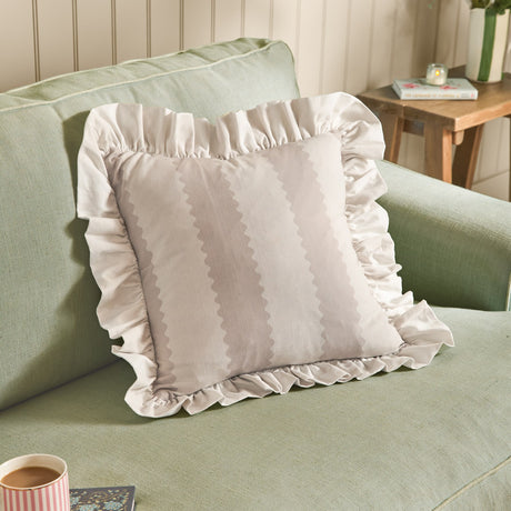 Birdie Stripe Frill Trim Cotton Cushion in natural, square with oatmeal striped scalloped design and gathered ruffle edge, shown on a sage green sofa.