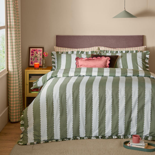 Bay green and off-white striped duvet cover set with scalloped edges and ruffle trim, styled with matching pillowcases and cushions on a bedroom bed.