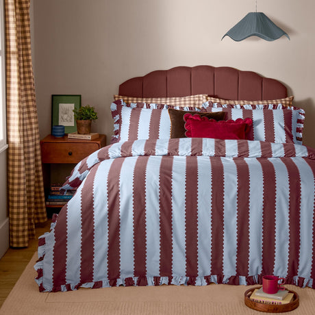 Birdie Stripe Printed Frill Trim Duvet Cover Set in blue and chocolate on a bed with matching pillowcases, ruffled edges, and gingham-check reverse, styled in a bedroom.