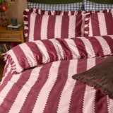 Birdie Stripe Frill Trim Duvet Cover Set in burgundy and blossom pink, showing bold zigzag-edged stripes with ruffled trim on the duvet and pillowcases, styled on a bed in a bedroom setting.
