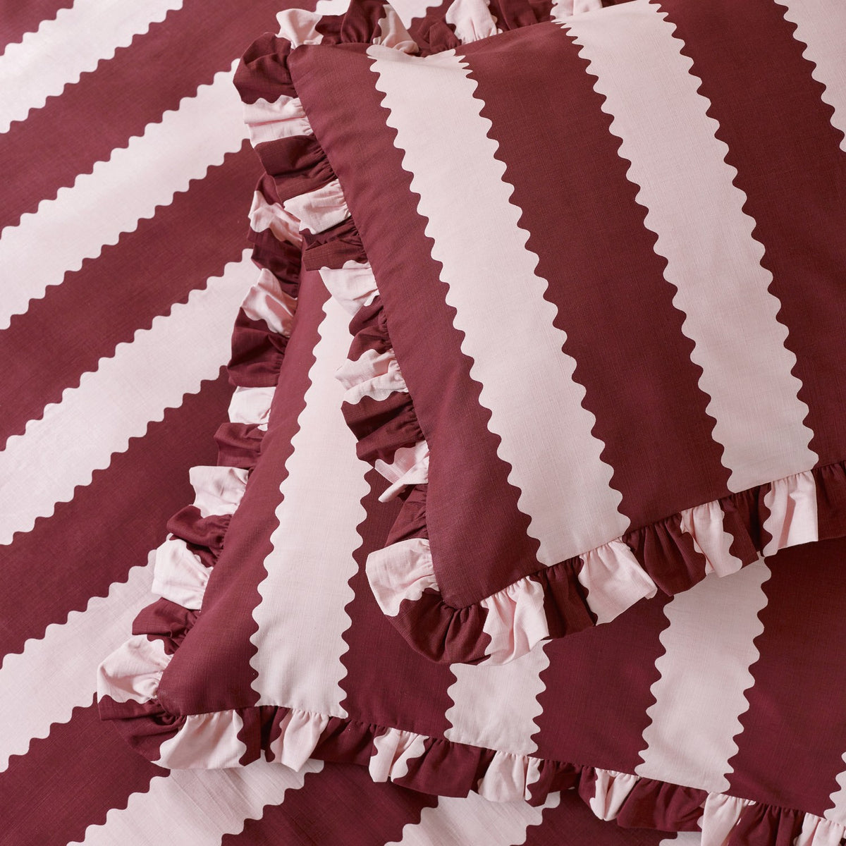 Birdie Stripe Frill Trim Duvet Cover Set in Burgundy/Blossom, showing bold diagonal stripes with zigzag edges and ruffled trim on the cover and matching pillowcases.
