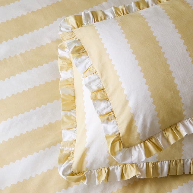 Birdie Stripe cotton blend pillowcase pair in butter yellow, featuring broad zigzag-edged stripes and a gathered ruffle trim, shown layered on matching striped bedding.