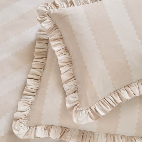 Birdie Stripe frill trim cotton blend pillowcase pair in natural, showing a subtle striped pattern with a gathered ruffle edge on a matching striped bedspread.