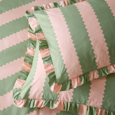 Birdie Stripe cotton blend pillowcase pair in pink and green, featuring a wavy scalloped stripe design with a gathered ruffle edge, shown layered on matching bedding.