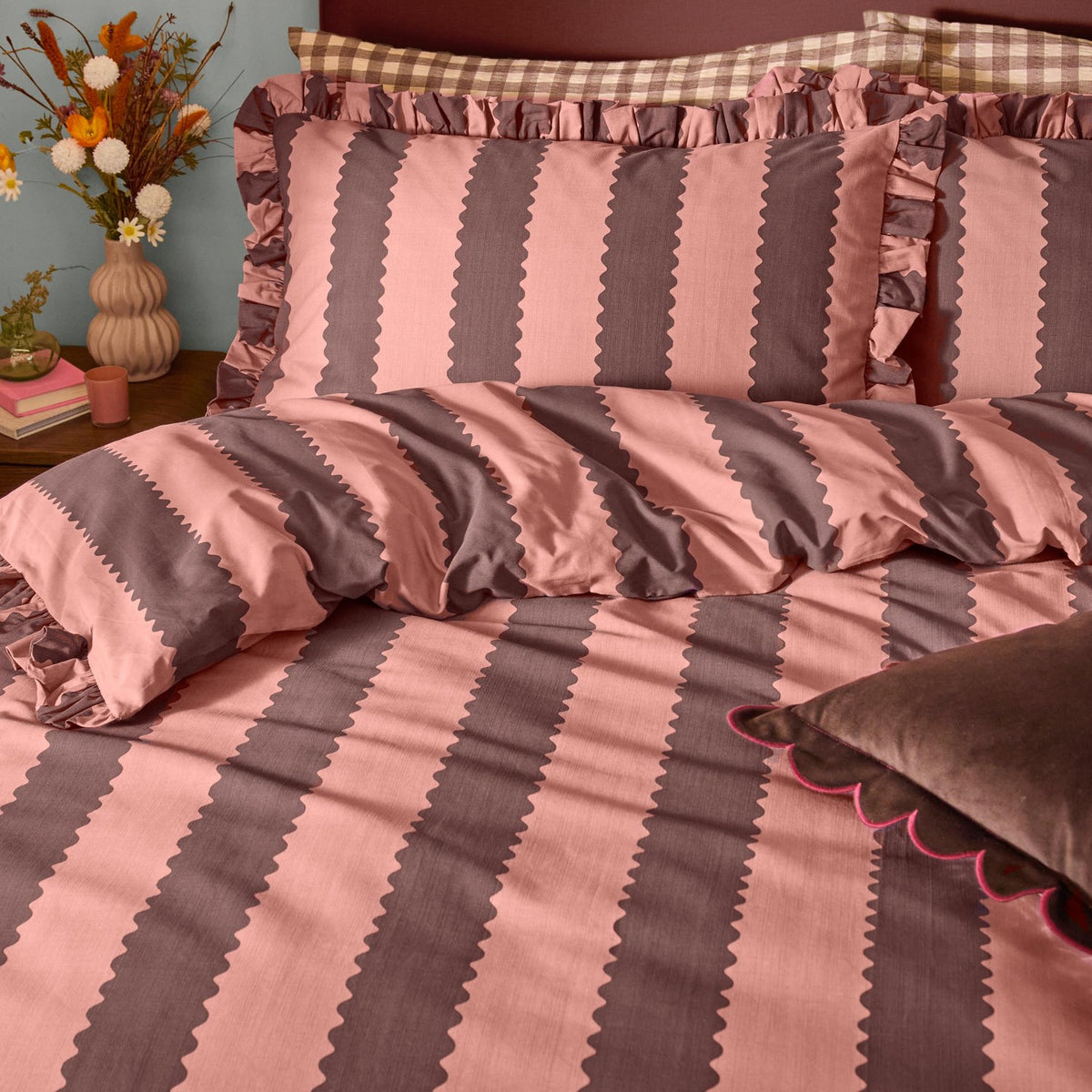 Birdie Stripe Cotton Blend Pillowcase Pair in rose and chocolate, featuring vertical scalloped stripes and a gathered ruffle edge, styled on a bed with checked shams.