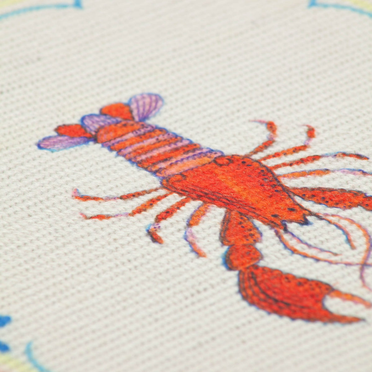 Close-up of a Brunch Stripes polyester placemat showing a digitally printed red lobster design in orange and purple thread-effect detail on a cream flatweave ground.