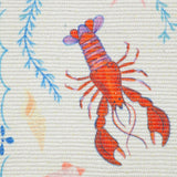 Close-up of the Brunch Stripes polyester table runner in cream, showing a printed red lobster with blue coral sprig details on woven fabric.