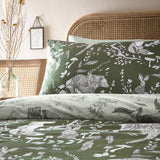 Buckthorn Reversible Animal Duvet Cover Set in Evergreen, showing woodland bear, fox, hare and foliage print in green and white on a rattan bed with linen pillowcase.