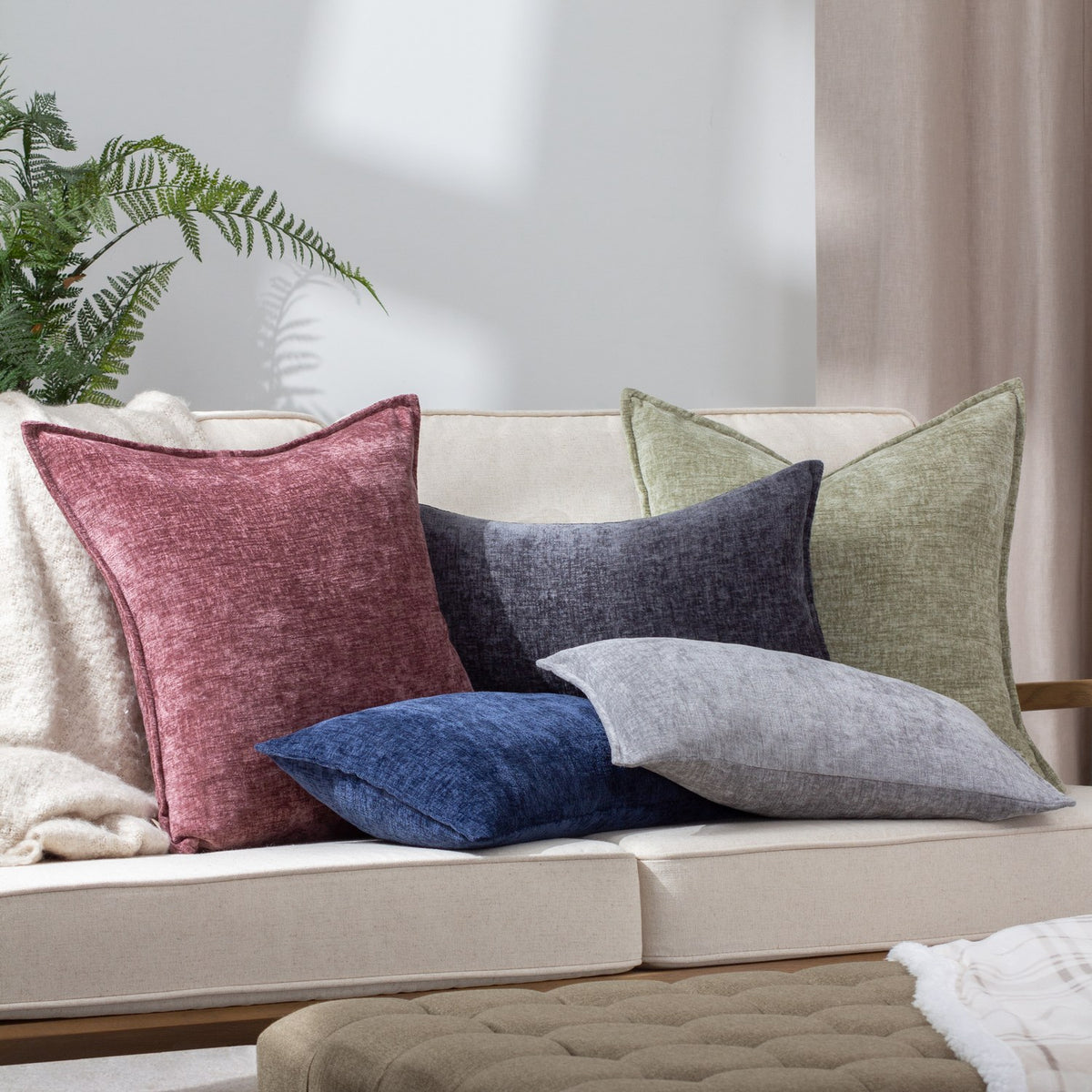 Buxton Reversible Polyester Cushions in charcoal grey chenille-style fabric styled with burgundy, navy and green square cushions on a cream sofa.