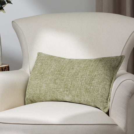 Buxton reversible rectangular cushion in eucalyptus green woven polyester, shown on a cream armchair in a living room setting.