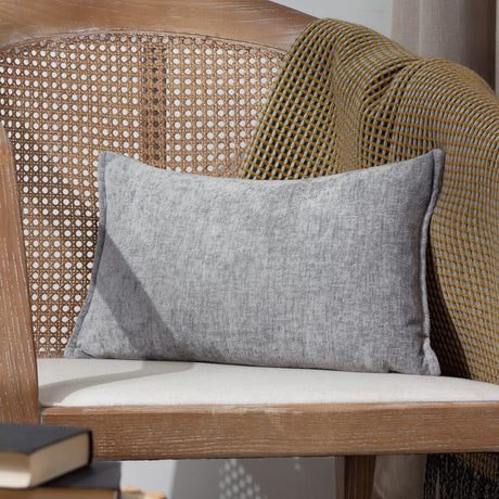 Buxton Reversible Polyester Cushion in grey, rectangular bolster shape with textured woven fabric, shown on a cane-back wooden chair.