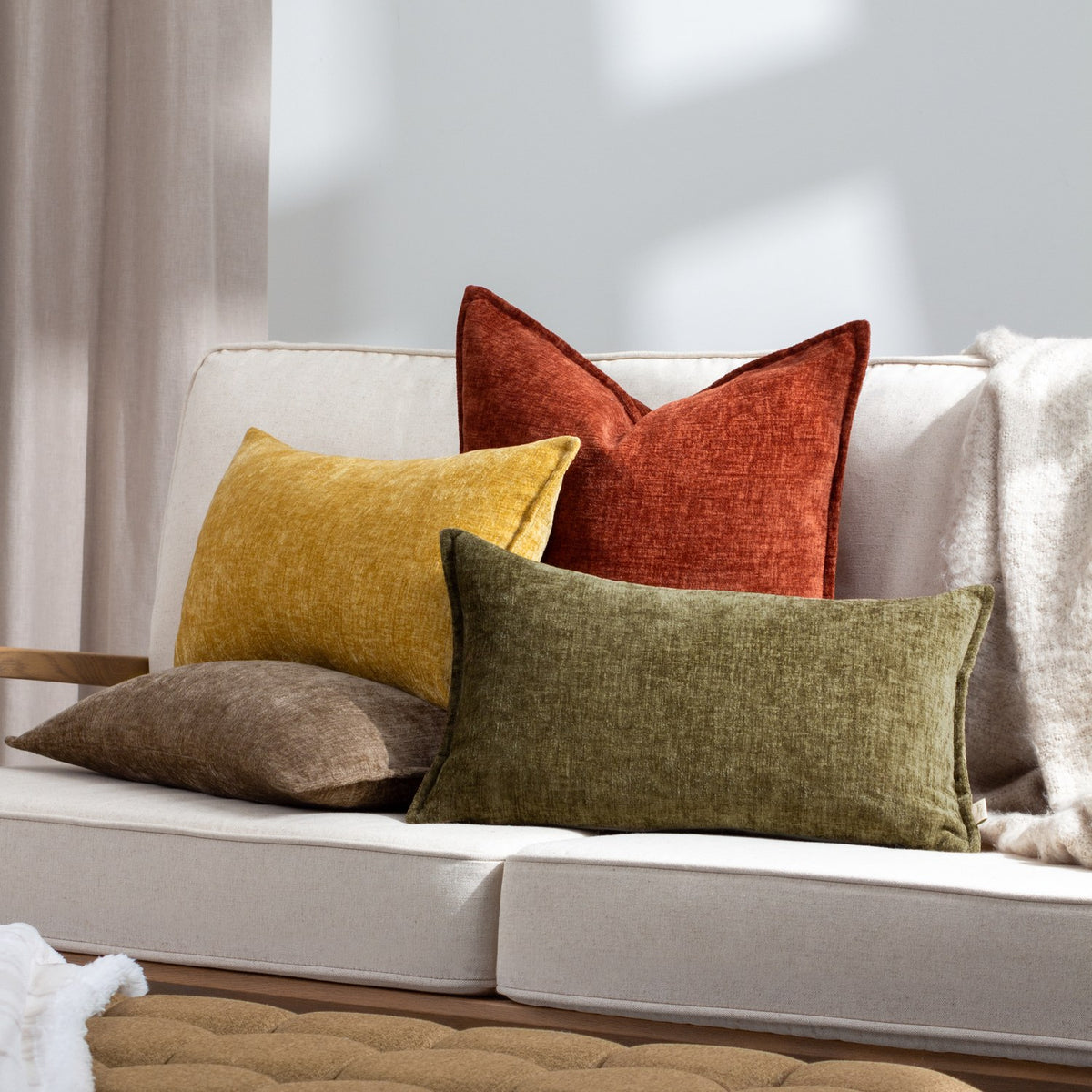 Buxton Reversible Polyester Cushion in ochre yellow, rectangular with a woven chenille-like texture, styled on a cream sofa alongside terracotta, olive and taupe cushions.