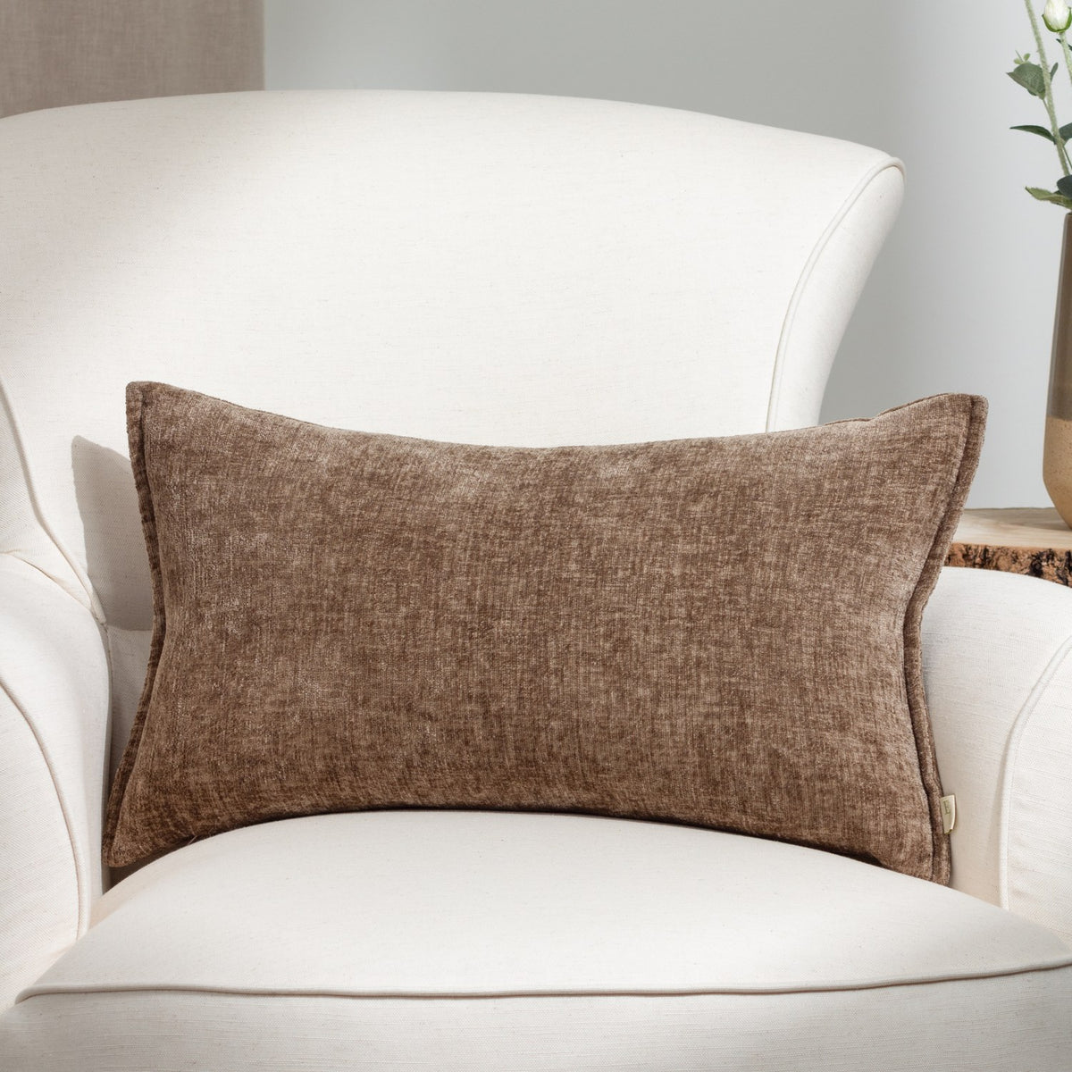 Buxton reversible rectangular scatter cushion in taupe chenille-like woven polyester, shown on a white armchair in a living room setting.