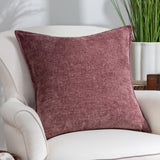 Buxton Reversible Polyester Cushion in Heather, a square textured chenille-style cushion in deep wine to soft rose tones, shown on a cream armchair beside a plant.