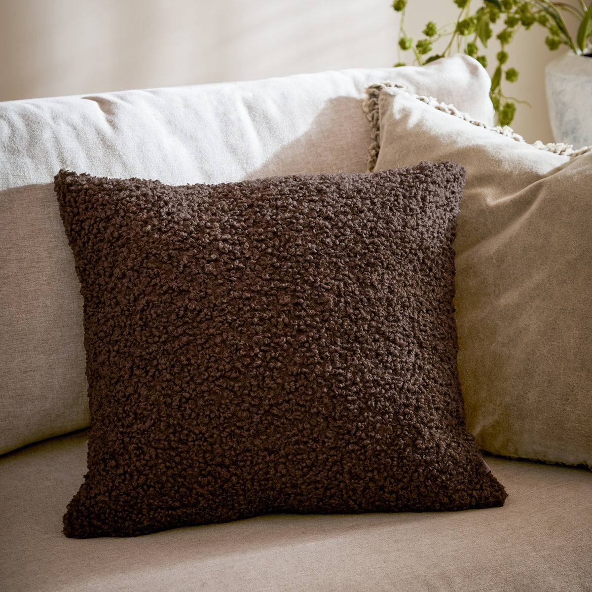 Cabu Plain Polyester Cushion in dark chocolate brown boucle texture, square shape, styled on a beige sofa with cream cushions in a living room setting.