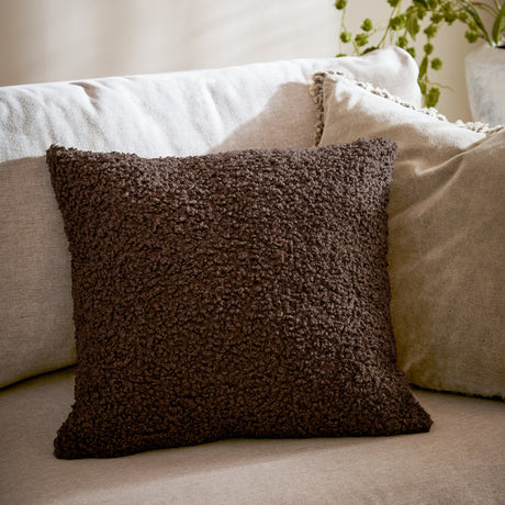 Cabu Plain Polyester Cushion in dark chocolate brown boucle texture, square shape, styled on a beige sofa with cream cushions in a living room setting.