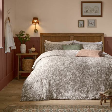Cademuir Cotton Woodland Duvet Cover Set in nut brown with off-white toile print, styled on a bed with pillows in a rustic bedroom featuring a rattan headboard.