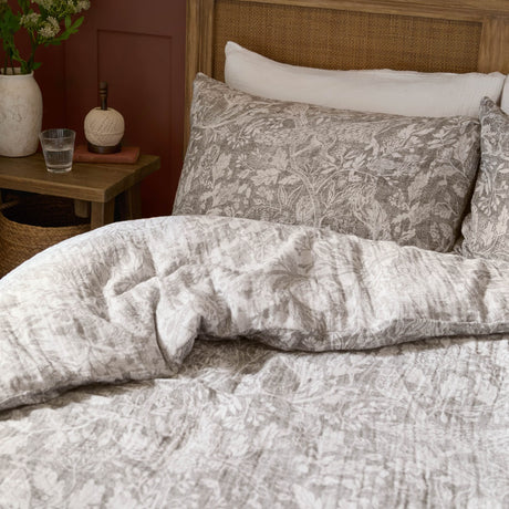 Cademuir cotton duvet cover set in nut brown, shown on a bed with matching pillowcases in a woodland toile print, styled in a bedroom with rattan headboard.