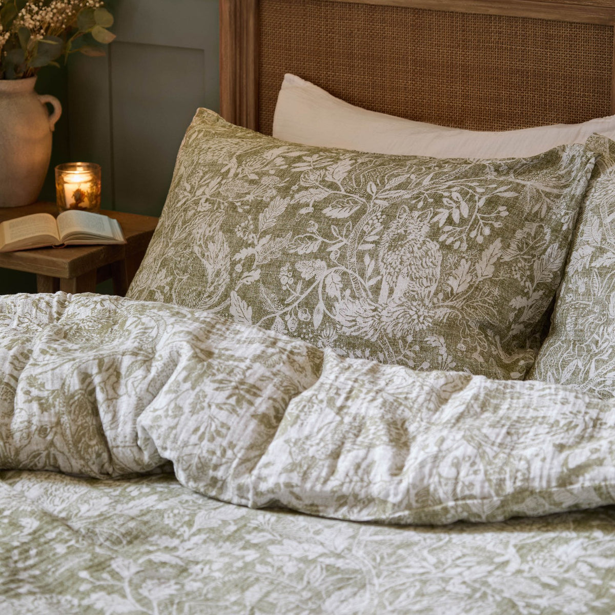 Cademuir Cotton Woodland Duvet Cover Set in sage green with white toile-style bird, hare and leaf print, shown on a bed with a matching patterned pillowcase.