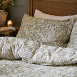 Cademuir Cotton Woodland Duvet Cover Set in sage green with white toile-style bird, hare and leaf print, shown on a bed with a matching patterned pillowcase.