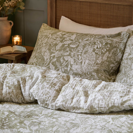 Cademuir Cotton Woodland Duvet Cover Set in sage green with white toile-style bird, hare and leaf print, shown on a bed with a matching patterned pillowcase.