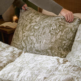 Cademuir Cotton Woodland Duvet Cover Set in sage being arranged on a bed, showing the white woodland toile print of birds, hares and leaves on a sage green cotton muslin ground.