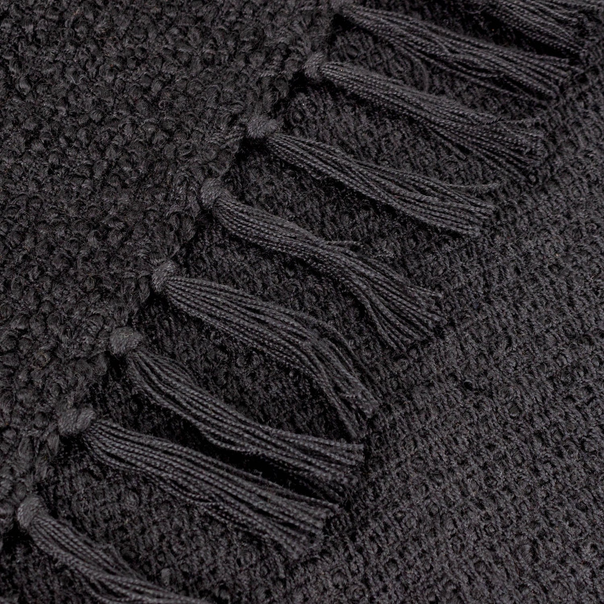 Close-up of the Candar Plain Polycotton Throw in black, showing looped boucle-woven texture with a hand-knotted fringe edge.