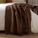 Candar Plain Polycotton Throw in cocoa brown, a boucle-woven textured blanket with knotted fringe ends, draped over a white bed in a bedroom setting.