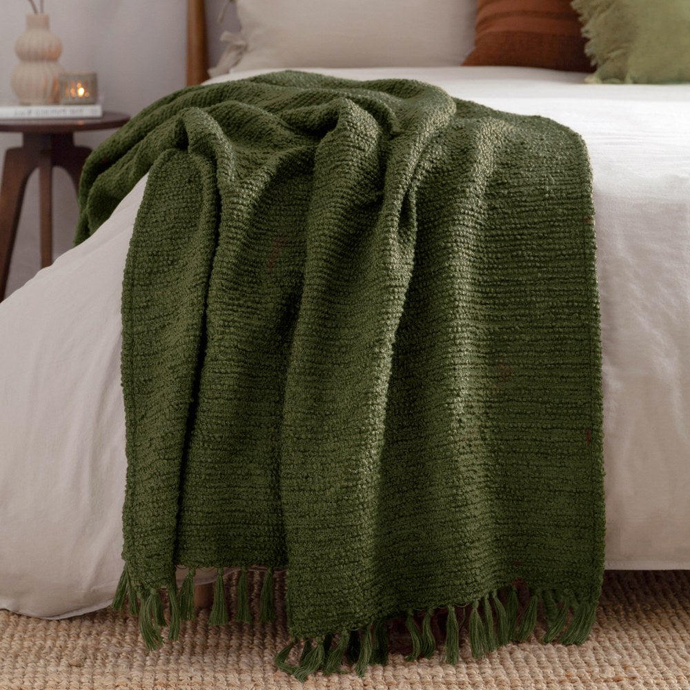 Candar Plain Polycotton Throw in khaki green, boucle-textured with fringed edges, draped over a white bed in a bedroom setting.