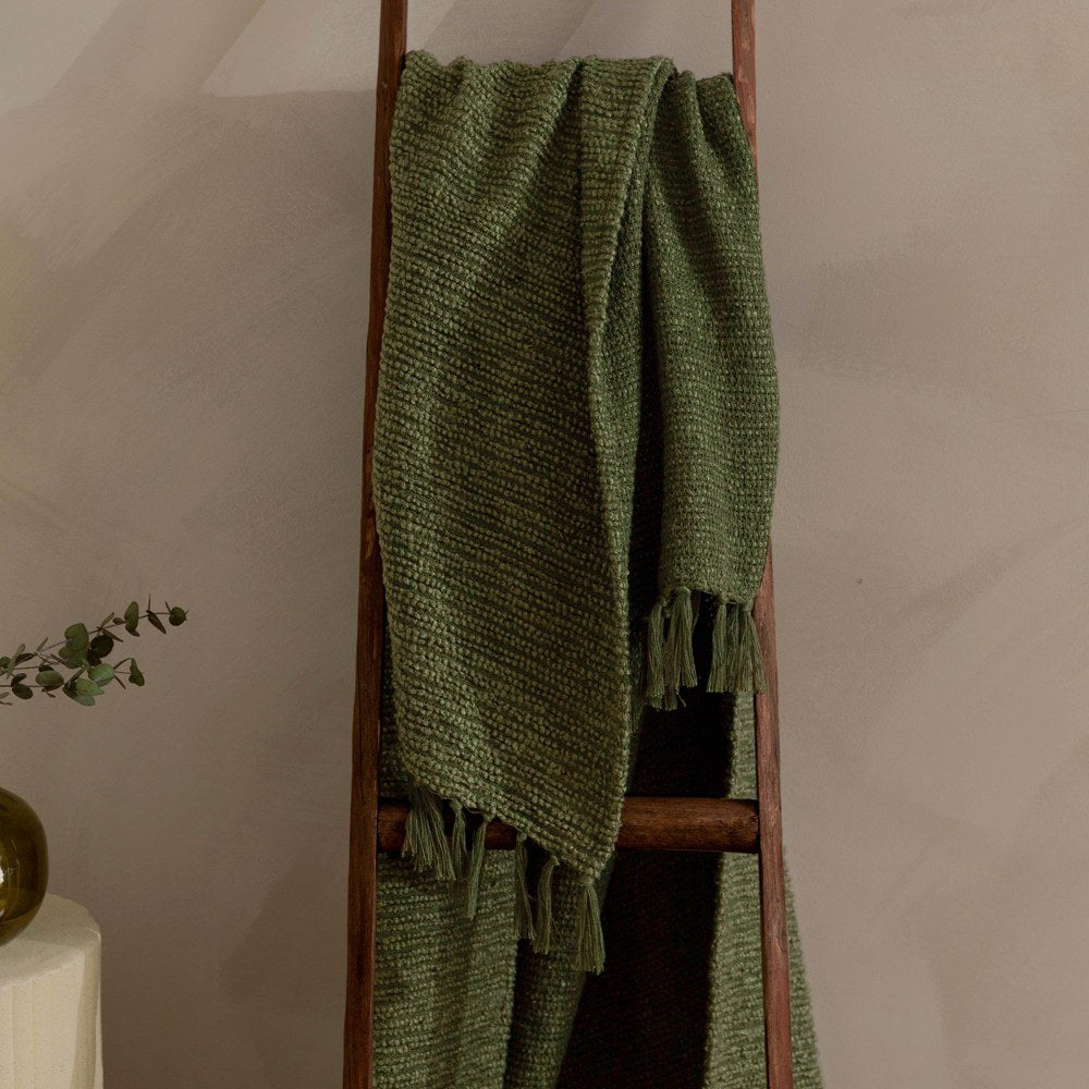 Candar Plain Polycotton Throw in khaki green, boucle-textured with fringed edges, draped over a wooden ladder against a neutral wall.