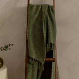 Candar Plain Polycotton Throw in khaki green, boucle-textured with fringed edges, draped over a wooden ladder against a neutral wall.