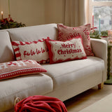 Square tufted cotton cushion with pink candy cane pattern on a cream sofa, styled with Fa La La La and Merry Christmas cushions in a festive living room.